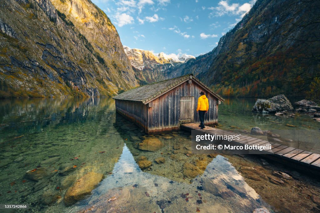 Person walking towards a boathouse in mountain lake, Germany