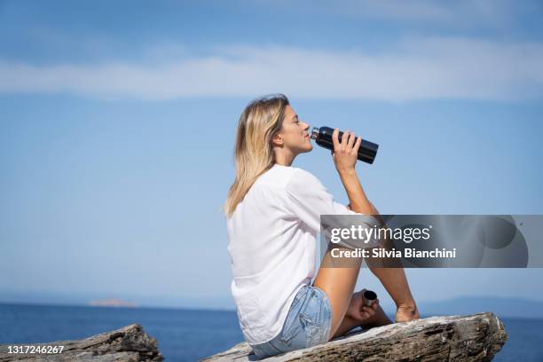 woman sitted on rocky cliff in front of the blue sea - beach drink stock pictures, royalty-free photos & images