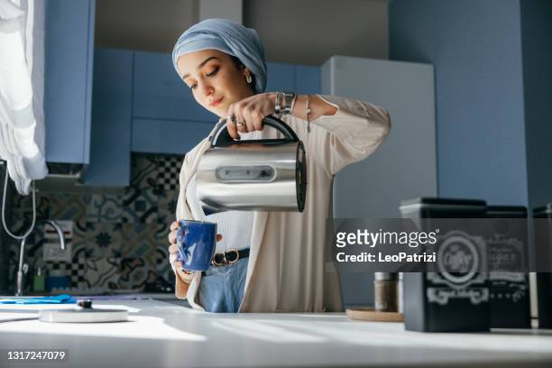 jeune femme préparant la caissière chaude de thé pour le petit déjeuner - bouilloire photos et images de collection