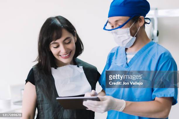 un dentista señala la pantalla de una tableta que muestra a su paciente, que sonríe. - doctor paciente stockfoto's en -beelden