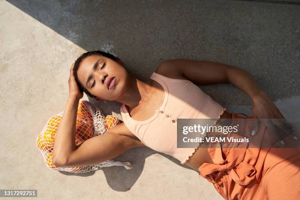 young short hair woman lying on the floor dressed in orange crop top and pants touching her hair on a bag full of oranges. - femme main ventre photos et images de collection