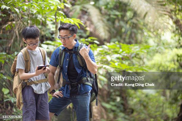 aziatische chinese vader en zoon die mobiele app op kaart voor richtingnavigatie gebruiken die bos wandelen en verkennen - malaysia father and son stockfoto's en -beelden