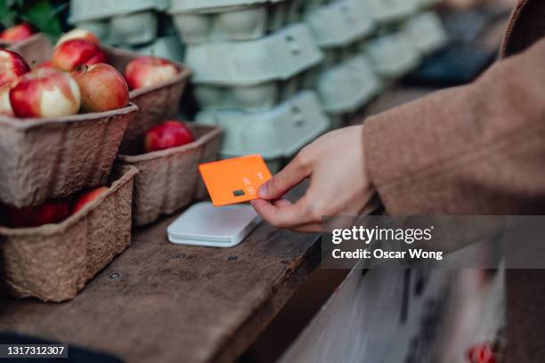 woman using credit card to pay for her shopping with contactless payment card reader in an outdoor food market - apple credit card stock pictures, royalty-free photos & images