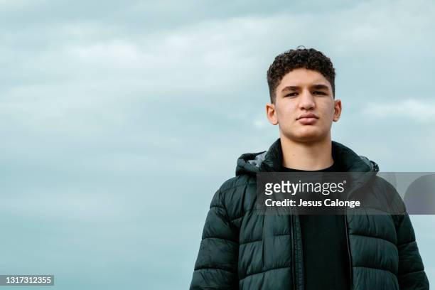 portrait of a latin teenager with hood on, looking at the camera with a serious expression. with a sky in the background. adolescents, problems and psychology concept. copyspace - one teenage boy only fotografías e imágenes de stock
