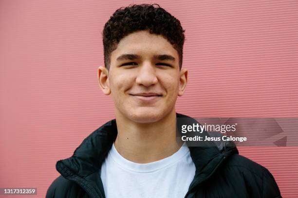 latin teenager with acne on his face, looking at the camera. with a red wall of the street in the background. teenagers and acne concept - spain teen face stock-fotos und bilder