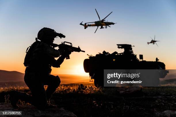 slagveld met een militair, gepantserd voertuig en vliegende helikopters bij zonsondergang - apache helikopter stockfoto's en -beelden