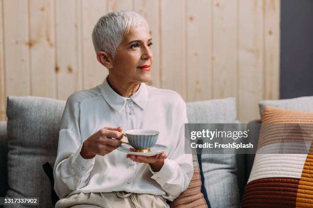 après-midi lent : verticale d’une femme aînée buvant le thé dans son salon - coupe pixie photos et images de collection