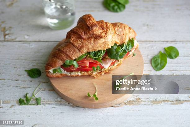 close-up of croissant with ham, tomato and leafy vegetables, idea of breakfast or lunch meal. - sandwich stock-fotos und bilder