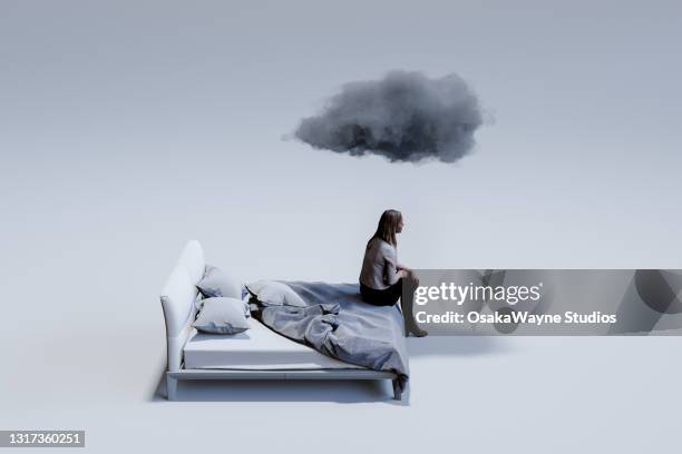 sad mid adult woman sitting on corner of double bed with dark cloud above head. - depressie stockfoto's en -beelden