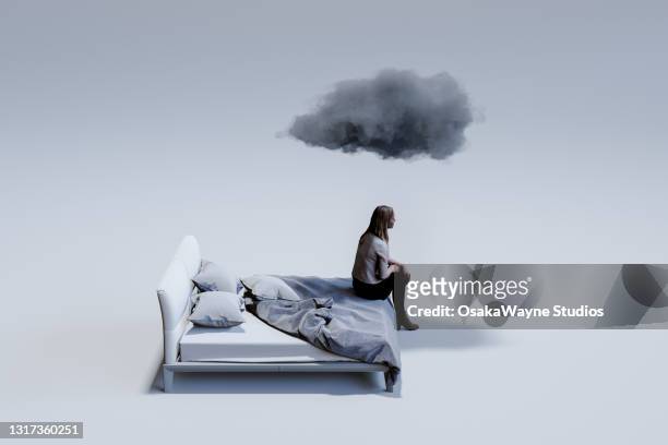sad mid adult woman sitting on corner of double bed with dark cloud above head. - emoção negativa imagens e fotografias de stock