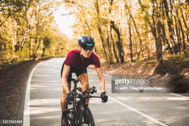 strength and concentrated professional sportswoman riding a triathlon bike by the road in autumn forest - triathlon cycling stock pictures, royalty-free photos & images