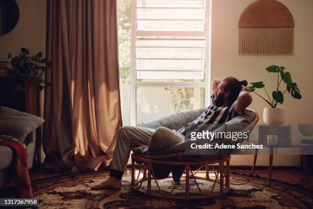 schuss eines jungen mannes, der sich zu hause auf einem stuhl entspannt - low key stock-fotos und bilder