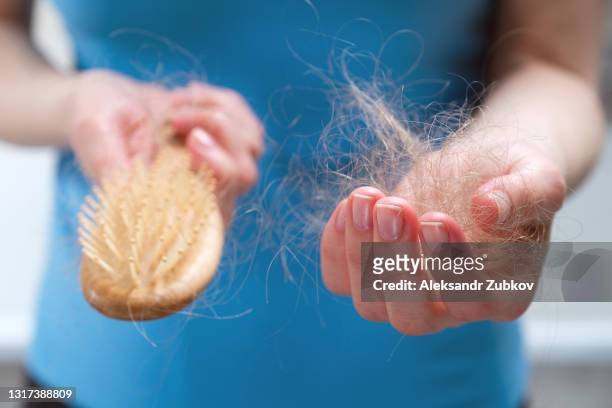 a woman holds a wooden comb in her hands, cleans it of fallen hair after combing. the concept of head health problems, deficient conditions in the body due to stress and depression, a consequence of chemotherapy and radiation for cancer. - haarausfall stock-fotos und bilder