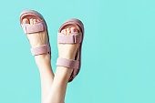 Female legs in pink sandals upside down on blue background.