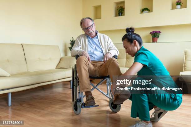 sorgfältige krankenschwester in zu hause besuch hilft einem behinderten senior mann im rollstuhl. - schuhpflege stock-fotos und bilder