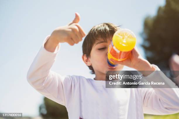 a happy child makes the ok symbol with the sky in the background while drinking industrial orange juice - only kids at sky stockfoto's en -beelden