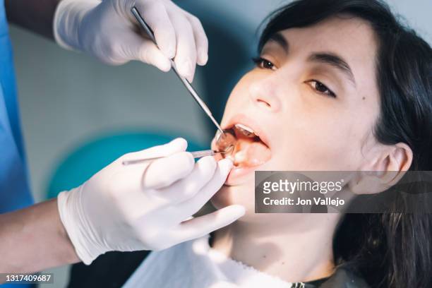 una paciente está siendo tratada por su dentista. el dentista le está limpiando los dientes con dos herramientas metálicas. - doctor paciente stockfoto's en -beelden