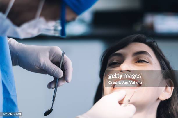 la joven cierra la boca apretando los dientes para que el dentista pueda ver si están bien encajados o no. el dentista agarra la barbilla de la paciente mientras sostiene una herramienta metálica en la otra mano. - mano en la barbilla - fotografias e filmes do acervo