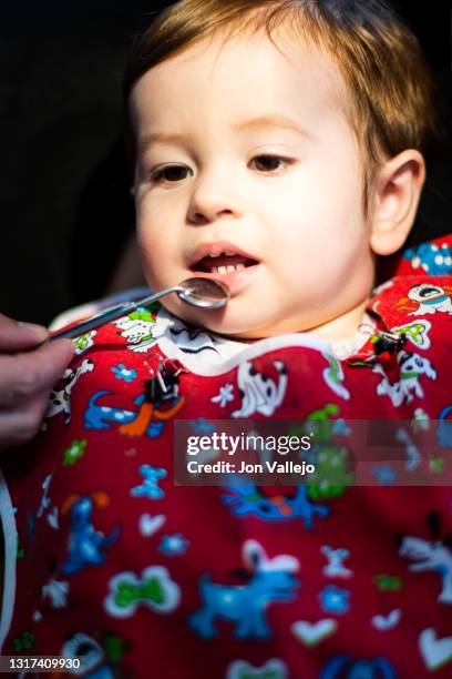 foto vertical de un niño menor de dos años en la consulta del dentista con una bata roja, el dentista está bajando el labio inferior del niño con un pequeño espejo. - 35 39 años stock pictures, royalty-free photos & images