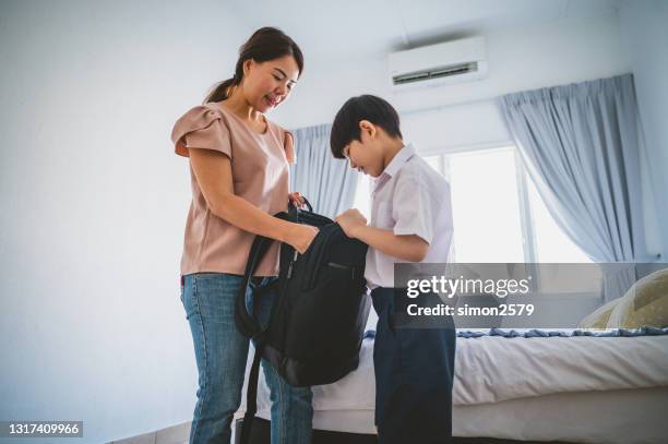 een aziatische moeder die rugzak voor haar zoon eerste dag van school inpakt - schoolbag lunchbox lunch stockfoto's en -beelden