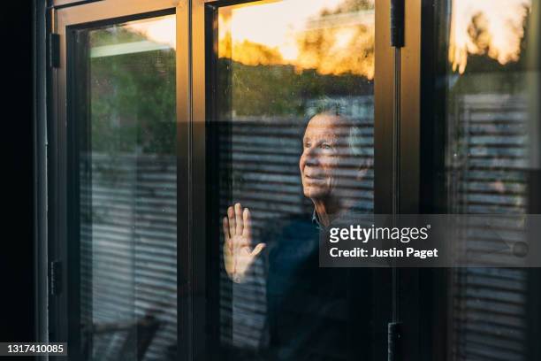 senior man looking out of his window at sunset - solitude stock pictures, royalty-free photos & images