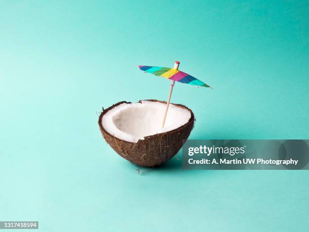 coconut with a cocktail umbrella on bright blue background - manufactured object stock pictures, royalty-free photos & images