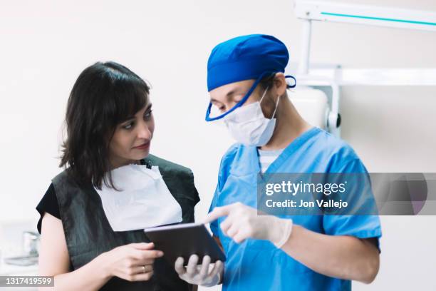 un dentista muestra a su paciente la pantalla de una tableta en su consulta. el dentista está señalando la pantalla mientras el paciente observa al dentista. - tableta digital stock pictures, royalty-free photos & images