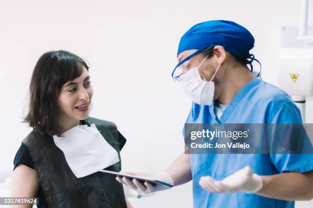 un dentista gesticula con una tableta en la mano mientras el paciente mira al dentista riéndose. - doctor paciente stockfoto's en -beelden