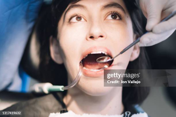 un dentista utiliza un espejo metálico y un tubo de succión de plástico en la boca de un paciente. - paciente stock pictures, royalty-free photos & images