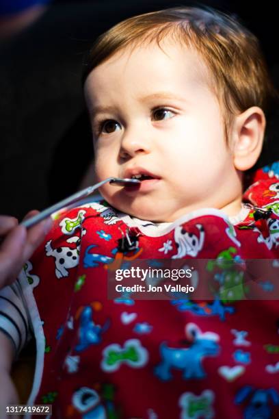 foto vertical de un niño menor de dos años en la consulta del dentista con una bata roja, el dentista está levantando el labio superior del niño con un pequeño espejo mientras el niño mira al dentista. - levantando photos et images de collection