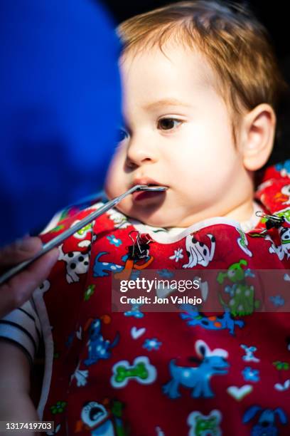 foto vertical de un niño menor de dos años en la consulta de un dentista con bata roja, el dentista está intentando abrir la boca del niño con un pequeño espejo mientras el niño mira al dentista. enfoque selectivo. - abrir 個照片及圖片檔