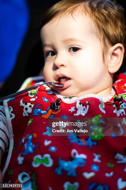 foto vertical de un niño menor de dos años en la consulta de un dentista con bata roja, el dentista está bajando el labio inferior del niño con un pequeño espejo para mirar sus dientes mientras el niño mira a la cámara. enfoque selectivo. - 35 39 años stock pictures, royalty-free photos & images