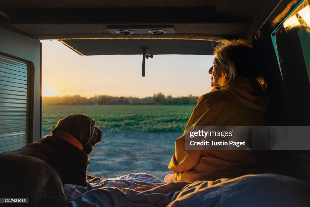 Senior woman and her pet dog looking at the view from the back of her campervan