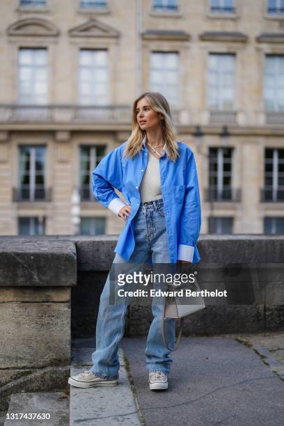 Xenia Adonts wears a blue oversized long shirt with white collar and white cuffs from Attire The Studio, a white ribbed asymmetric top from Attire...