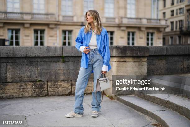 Xenia Adonts wears a blue oversized long shirt with white collar and white cuffs from Attire The Studio, a white ribbed asymmetric top from Attire...