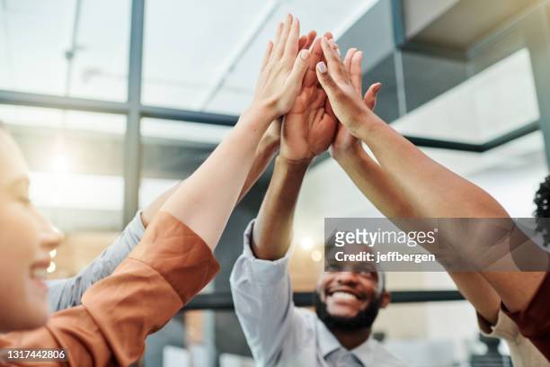 low angle shot of a group of businesspeople giving each other a high five in an office - hi five stock pictures, royalty-free photos & images