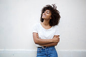 happy young african american woman smiling with arms crossed and looking away against white background