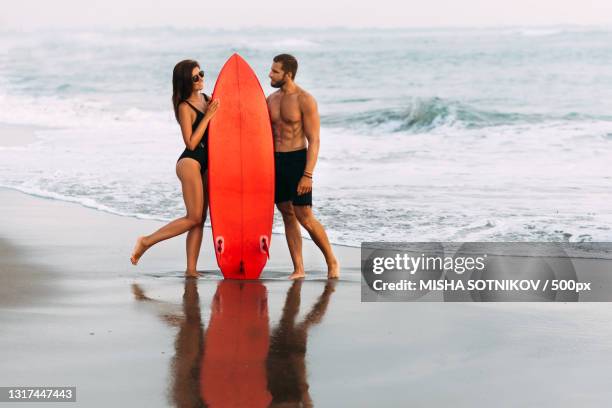 a couple in love on the beach with a red surfboard - surf board foto e immagini stock