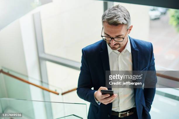 shot of a mature businessman using a cellphone while walking up a staircase in an office - man walking top view stock pictures, royalty-free photos & images