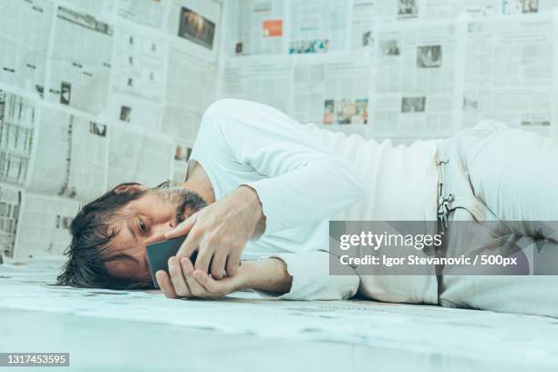 man lying on floor in a room covered in newspapers showing concept of misinformation and delusion - misinformation stock-fotos und bilder