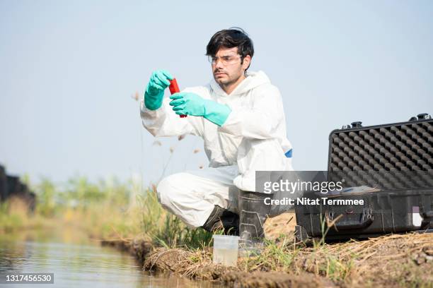 male scientist reading ph value or examining toxic water from a water sample. he working outdoors and wearing protective workware coveralls. water pollution and conservation and management of water concepts. - scientist full length stock pictures, royalty-free photos & images