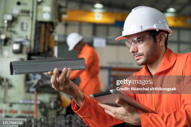 shot of manager inspector wearing protective quality control and analyzing piece of iron while using laptop in a factory. - siderurgicas fotografías e imágenes de stock
