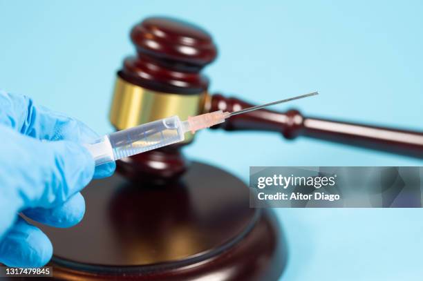 a person wearing surgical gloves holds a syringe. in the background a judge's gavel. - forbidden coronavirus stock pictures, royalty-free photos & images