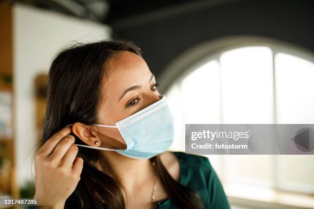 young woman putting on a protective face mask - máscara de proteção imagens e fotografias de stock
