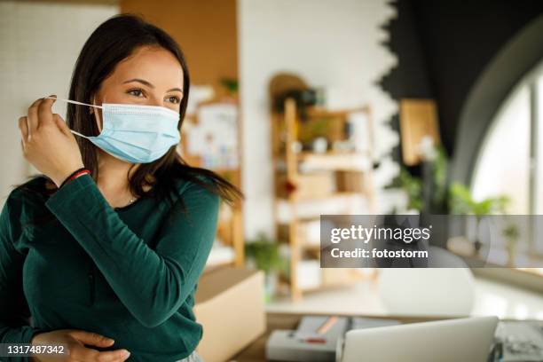 young woman looking away as she is taking off her protective face mask - removing surgical mask stock pictures, royalty-free photos & images