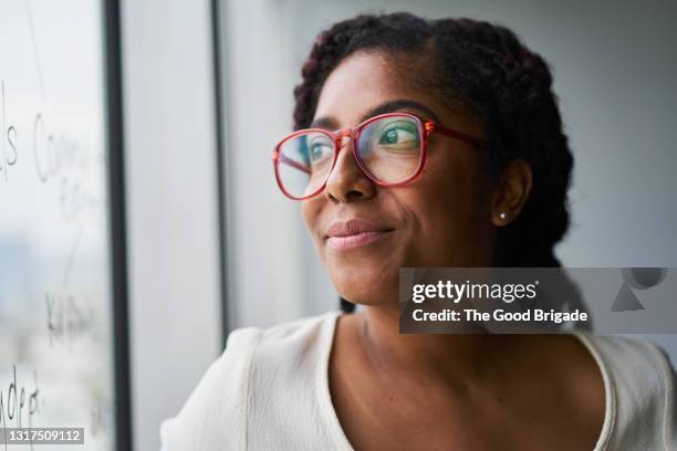 portrait of cheerful businesswoman looking out window in conference room - gafas de ver fotografías e imágenes de stock