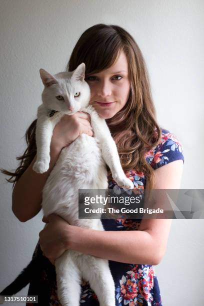 portrait of young woman carrying cat against gray background - cat studio stock pictures, royalty-free photos & images