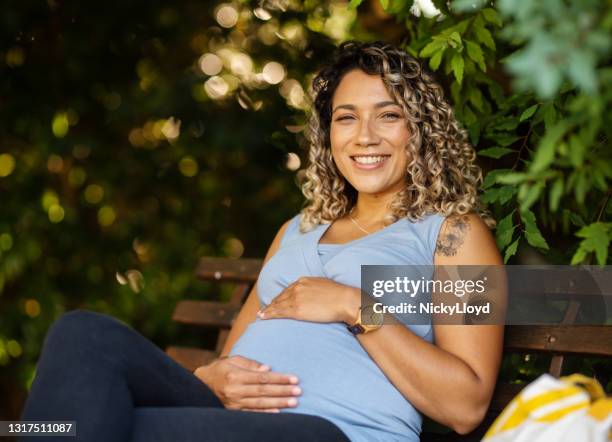 glimlachende jonge zwangere vrouwenzitting in openlucht op een parkbank - pregnant lady stockfoto's en -beelden