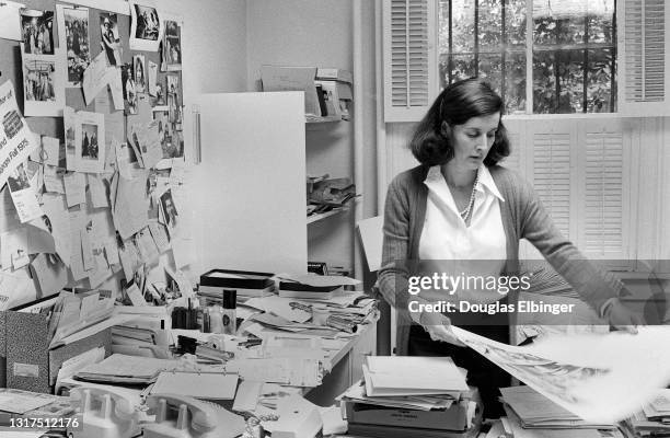 Portrait of American photographer and writer Jill Krementz as she sorts photographs on a crowded desk at her home, New York, New York, November 1975.