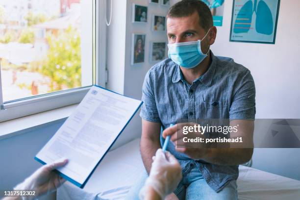 patient in schutzbetonter gesichtsmaske füllt papierkram in einer arztpraxis aus - erlaubt stock-fotos und bilder